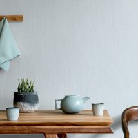Stylish and minimalistic dining room interior with wooden table, teapot with cups, plant and elegant accessories. Eucalyptus color. Ready to use. Template. Modern home decor. Copy space.